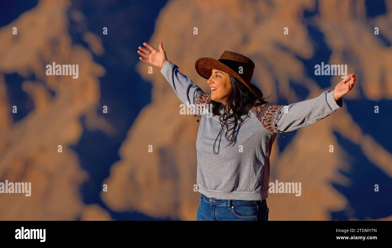 Young woman standing on a cliff at Grand Canyon and raising her arms ...
