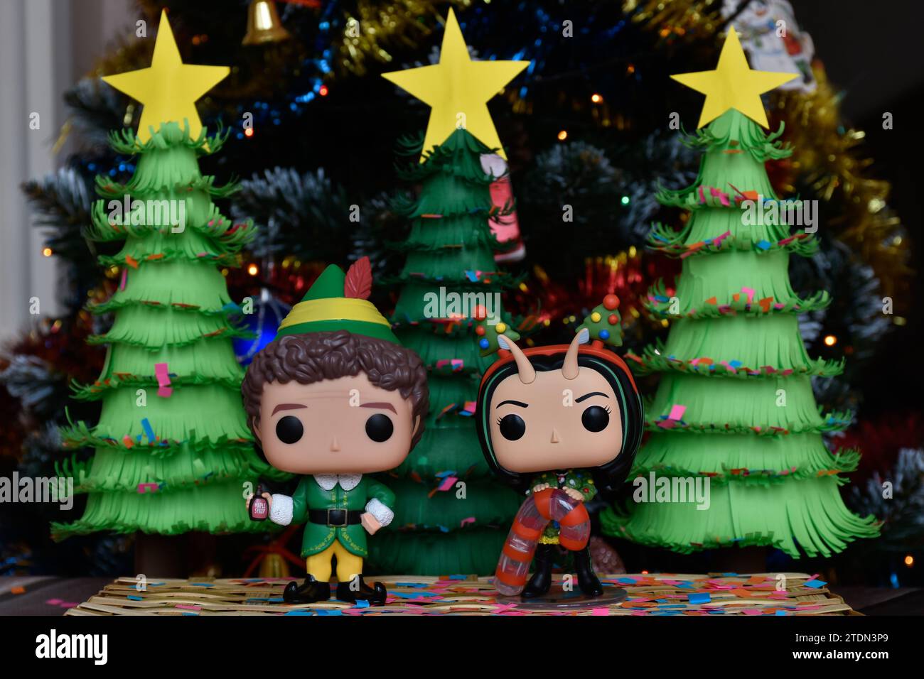 Funko Pop action figures of Buddy from movie Elf and Marvel superhero Mantis from Guardians of the Galaxy. Handmade paper Christmas trees, confetti. Stock Photo