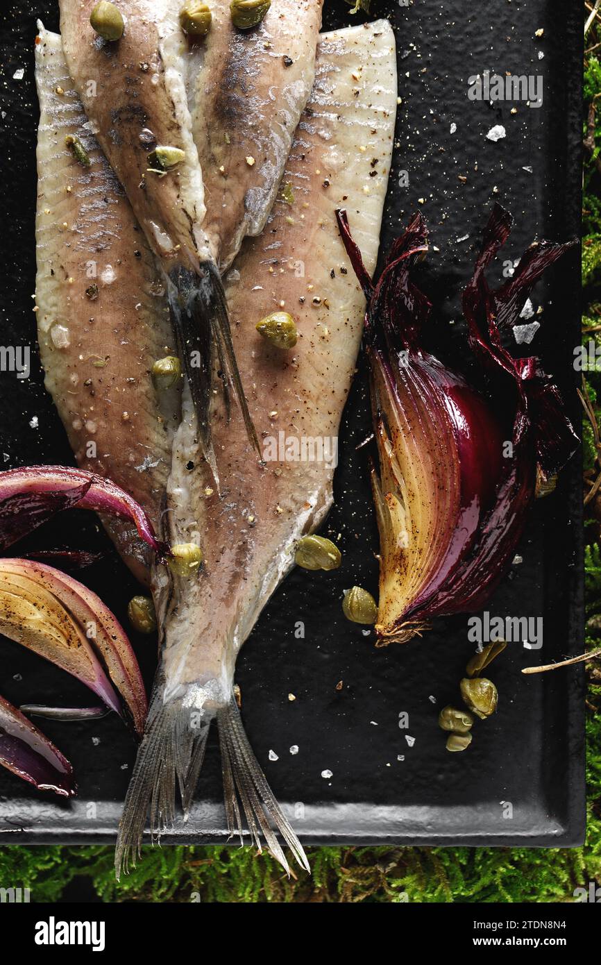 Herring fillet with capers, salt flakes, red onion and pepper served on black tray on green