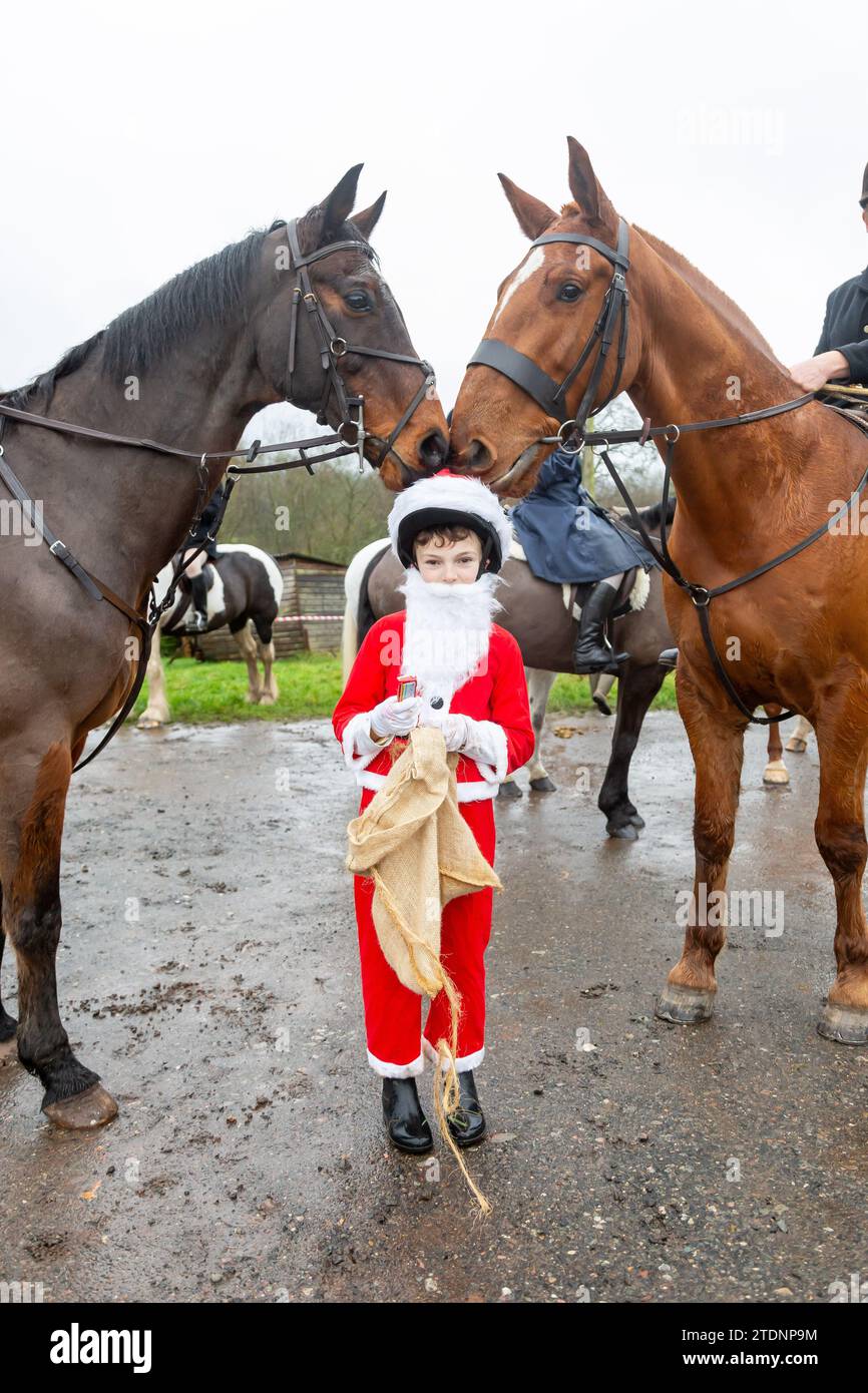 Upper Arley, Kidderminster, Worcestershire, UK. 19th Dec, 2023. Two horses nibble on 10-year-old Henley Mills' Santa hat as he hands out chocolate bars to members of the Albrighton and Woodland hunt as they have a lawn meet and trail ride from a farm in Upper Arley, near Kidderminster in Worcestershire. Credit: Peter Lopeman/Alamy Live News Stock Photo