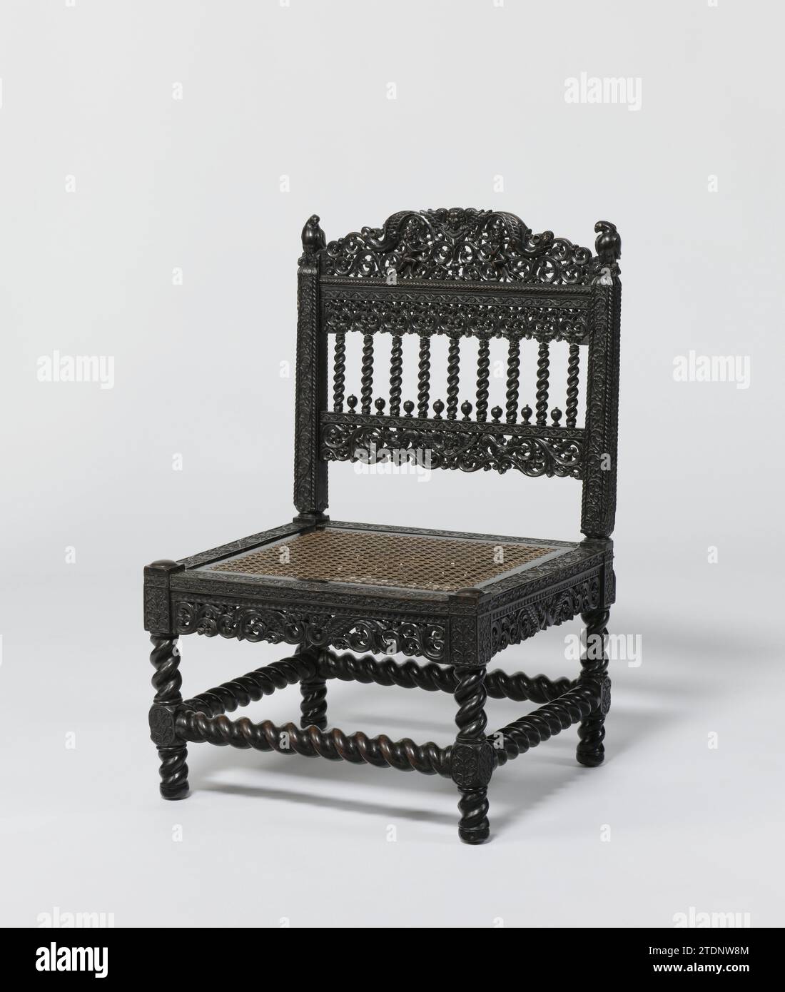 Chair with parrot -like birds, anonymous, c. 1650 - c. 1700 Low ebony chair with a loose seat, covered with rattan braid, flinged legs with houses and flinged rules. The houses, information rule and backstyles show rosettes and tenders. Under the seating rules openwork sculpture with two winged samples and tendrils. Parrot -like birds on the backstyles. Between the sills are nine -lined columns with leaf capitals, between which eight buds, are applied. The chair shows sculpture with, among other things, winged heads, female figures and samples. Sri Lanka wood (plant material). ebony (wood). ra Stock Photo
