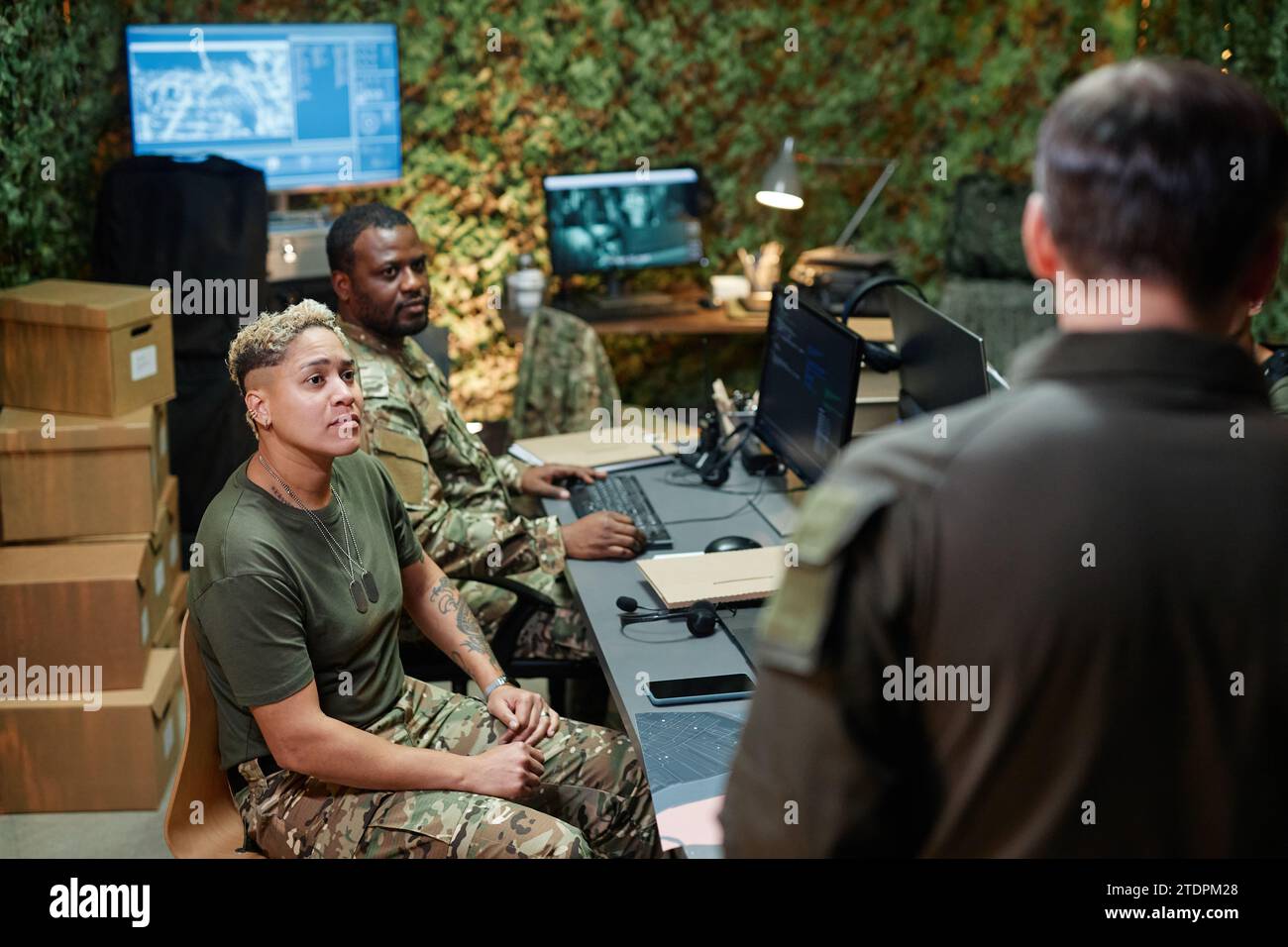 Group of young intercultural officers of surveillance room looking at male speaker or coach standing in front of them during report Stock Photo