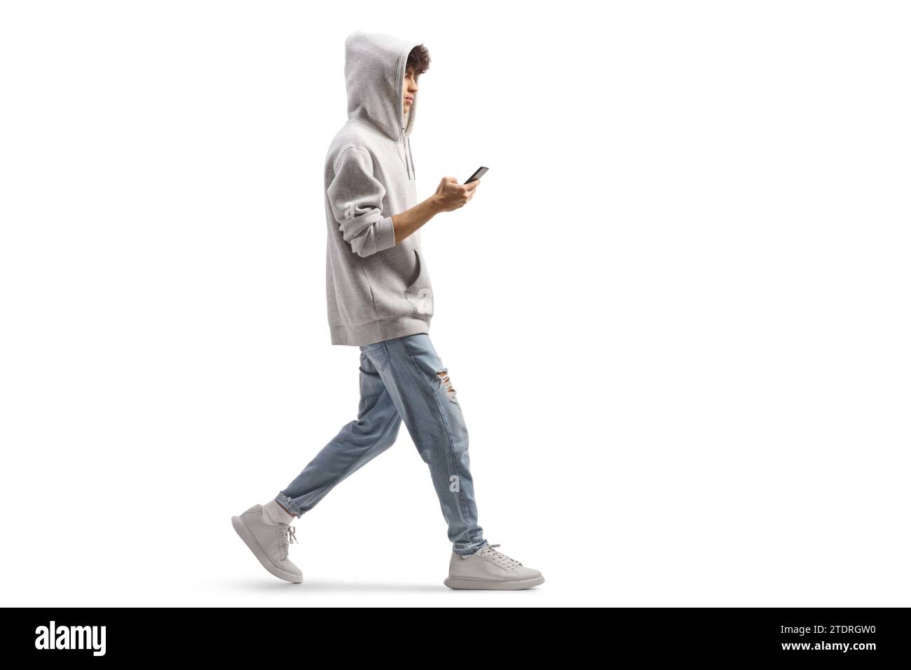 Full length shot of a guy wearing a gray hoodie and walking with a smartphone isolated on white background Stock Photo