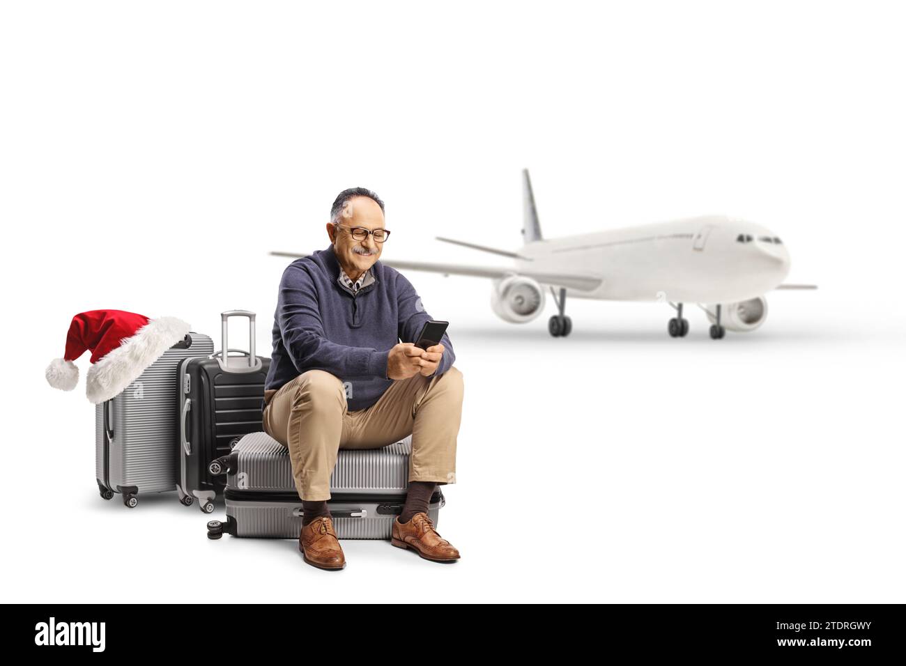 Mature man travelling for christmas, seated on a suitcase with a smartphone isolated on white background Stock Photo