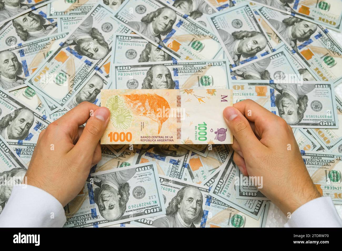 Hands Holding Argentinian Money Against $100 Bills Background. Economic Crisis In Argentina Stock Photo