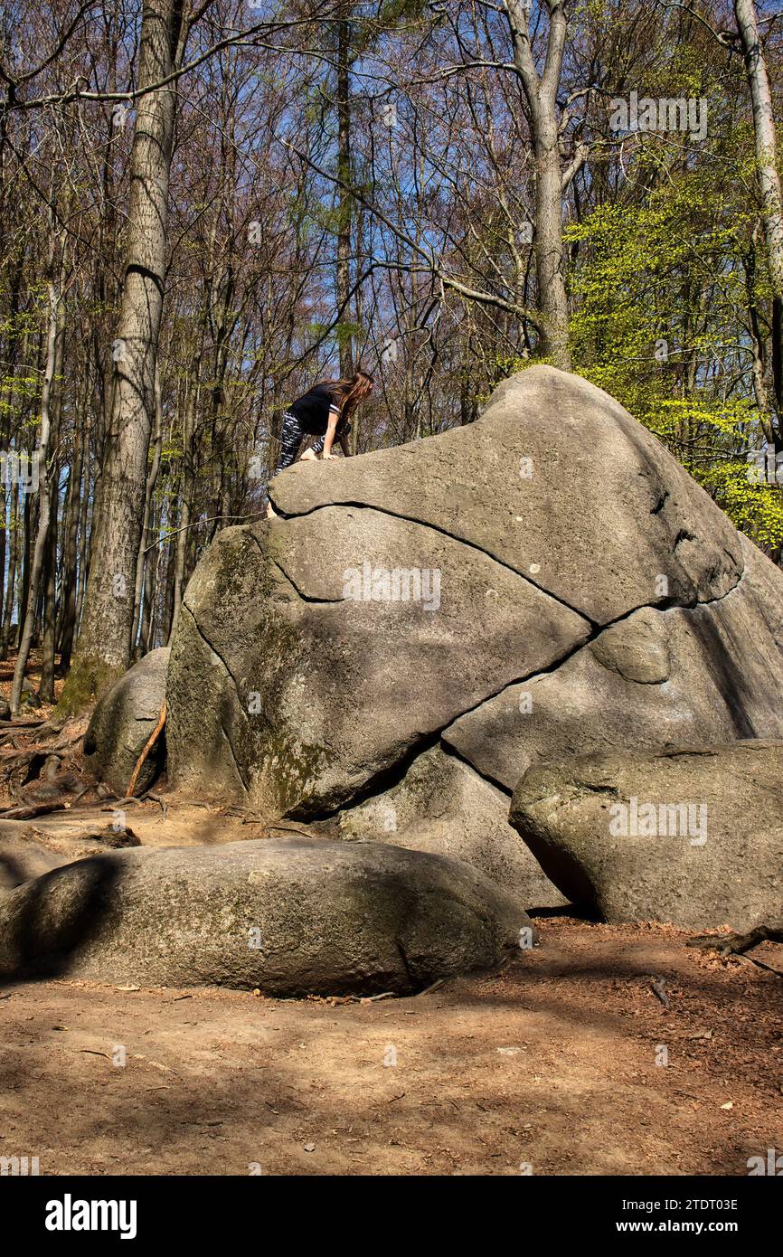Lautertal, Germany - April 24, 2021: Teenage girl climbing on a large rock at the top of Felsenmeer on a spring day in Germany. Stock Photo