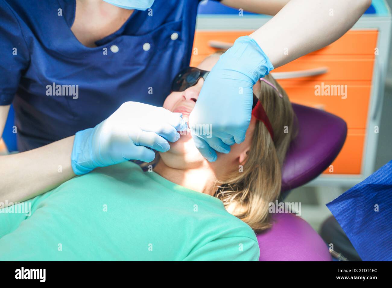 Little scared girl sitting in chair in dentist doctor office. Protective safety sunglasses. Kid,child afraid of tooth extraction, teeth treatment. Ope Stock Photo