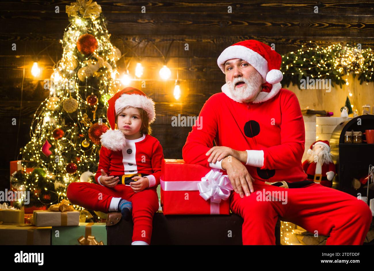 Christmastime. Santa man with little helper at home near Christmas tree. Family holidays. Santa Claus and Christmas child boy with gift box. Winter Stock Photo