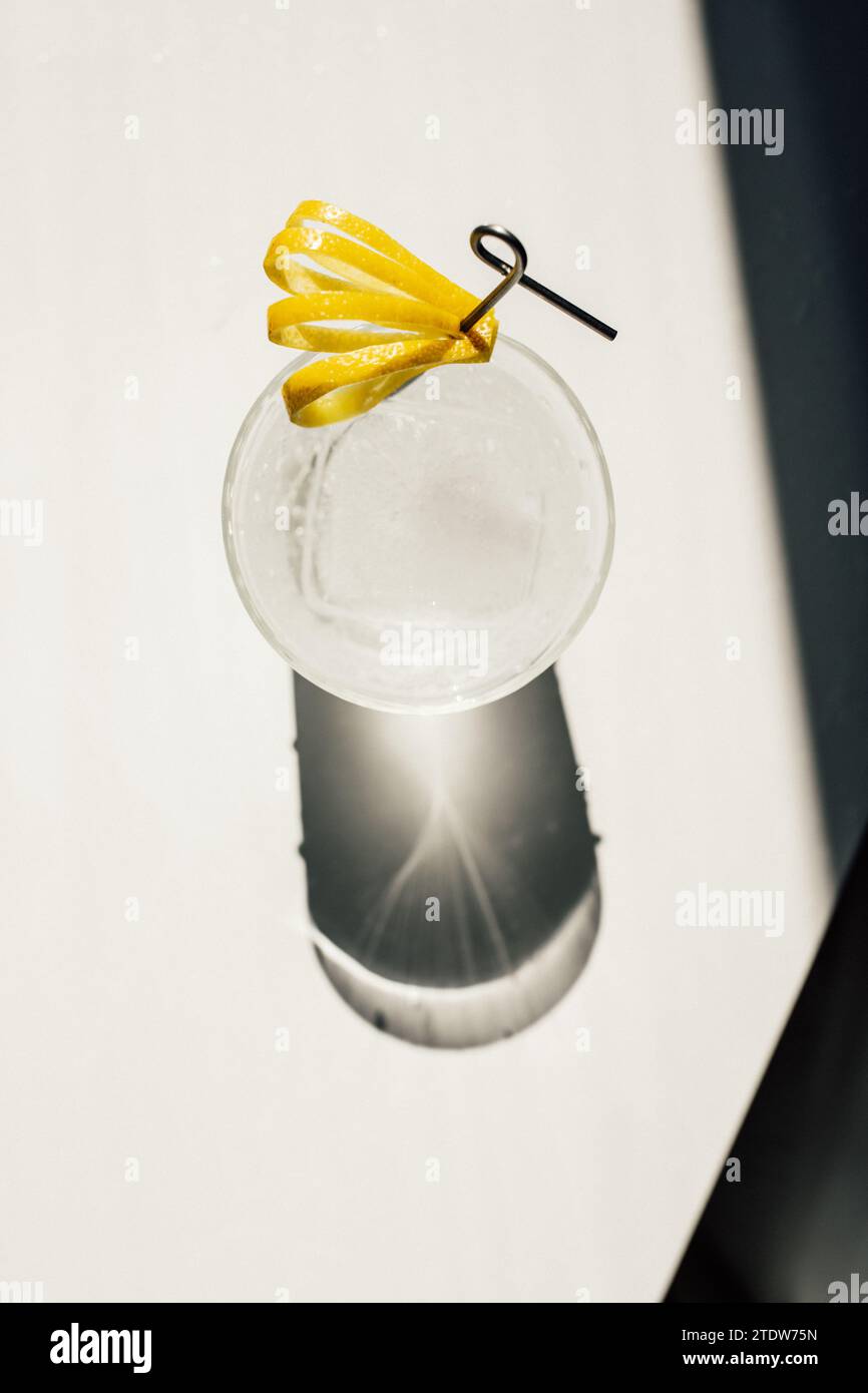 soda water with ice and cut lemon peel garnish on cocktail pick in the sun, white table Stock Photo