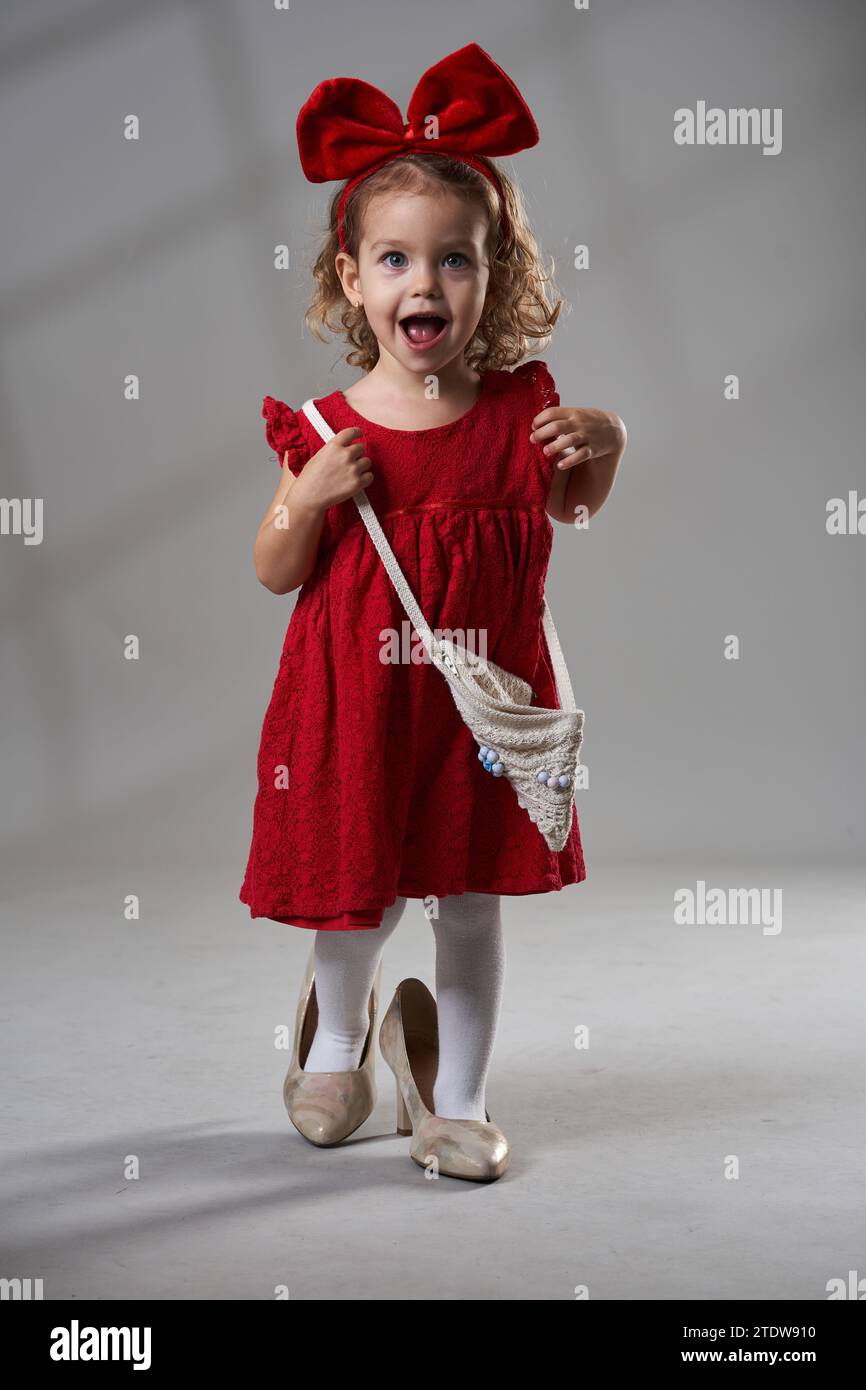 Portrait of an adorable blonde curly hair little girl in red dress and ...