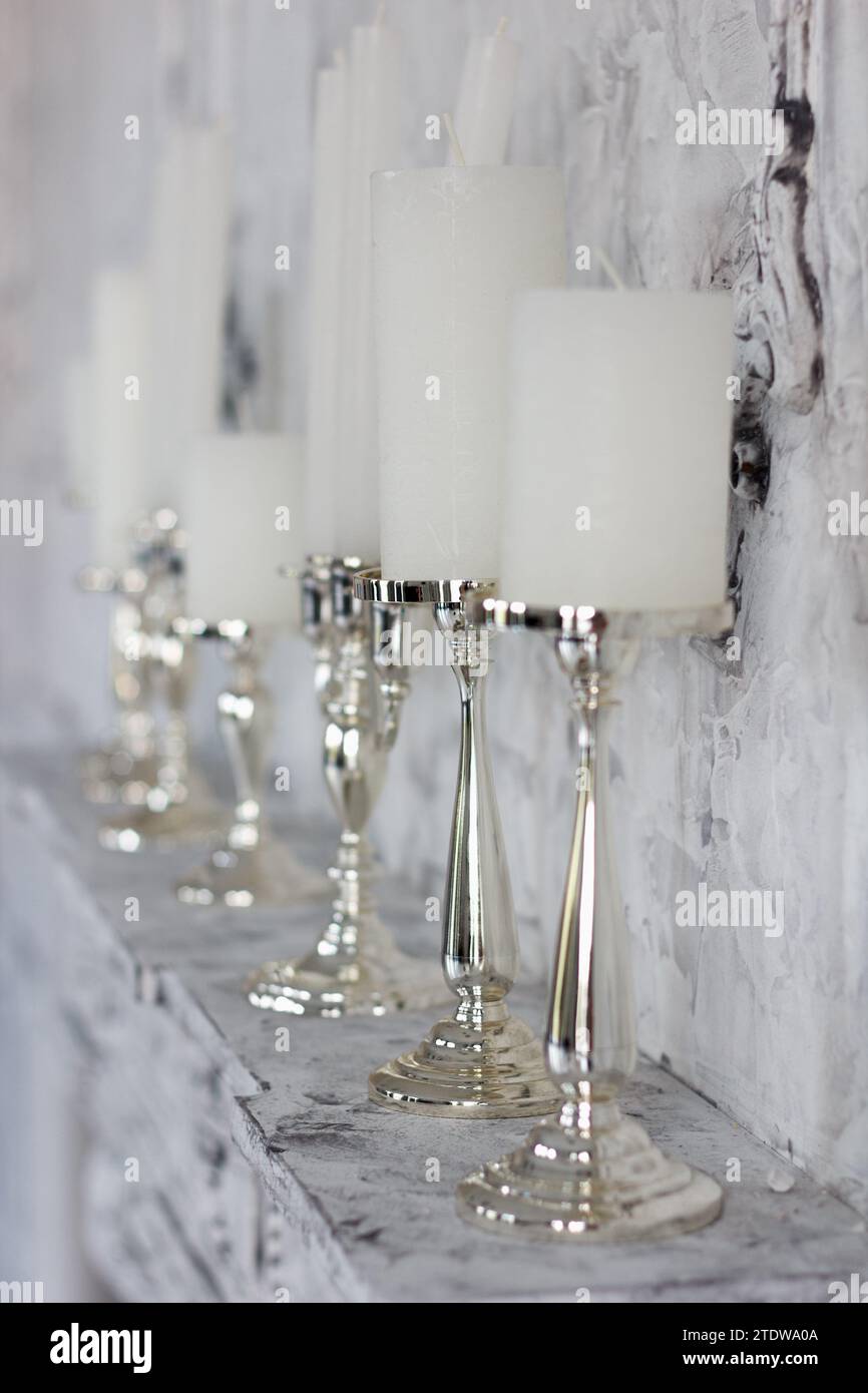 White beauty candles in elegant candlesticks stand on a fireplace in the room Stock Photo