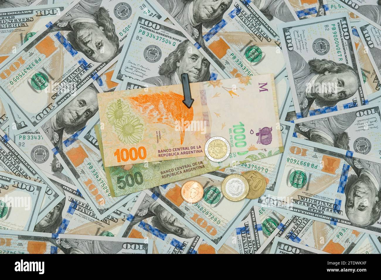 Argentina Banknotes And Coins With Black Arrow Heading Downward On US Dollars Background. Meaning The Devaluation Of The Argentine Peso. Stock Photo