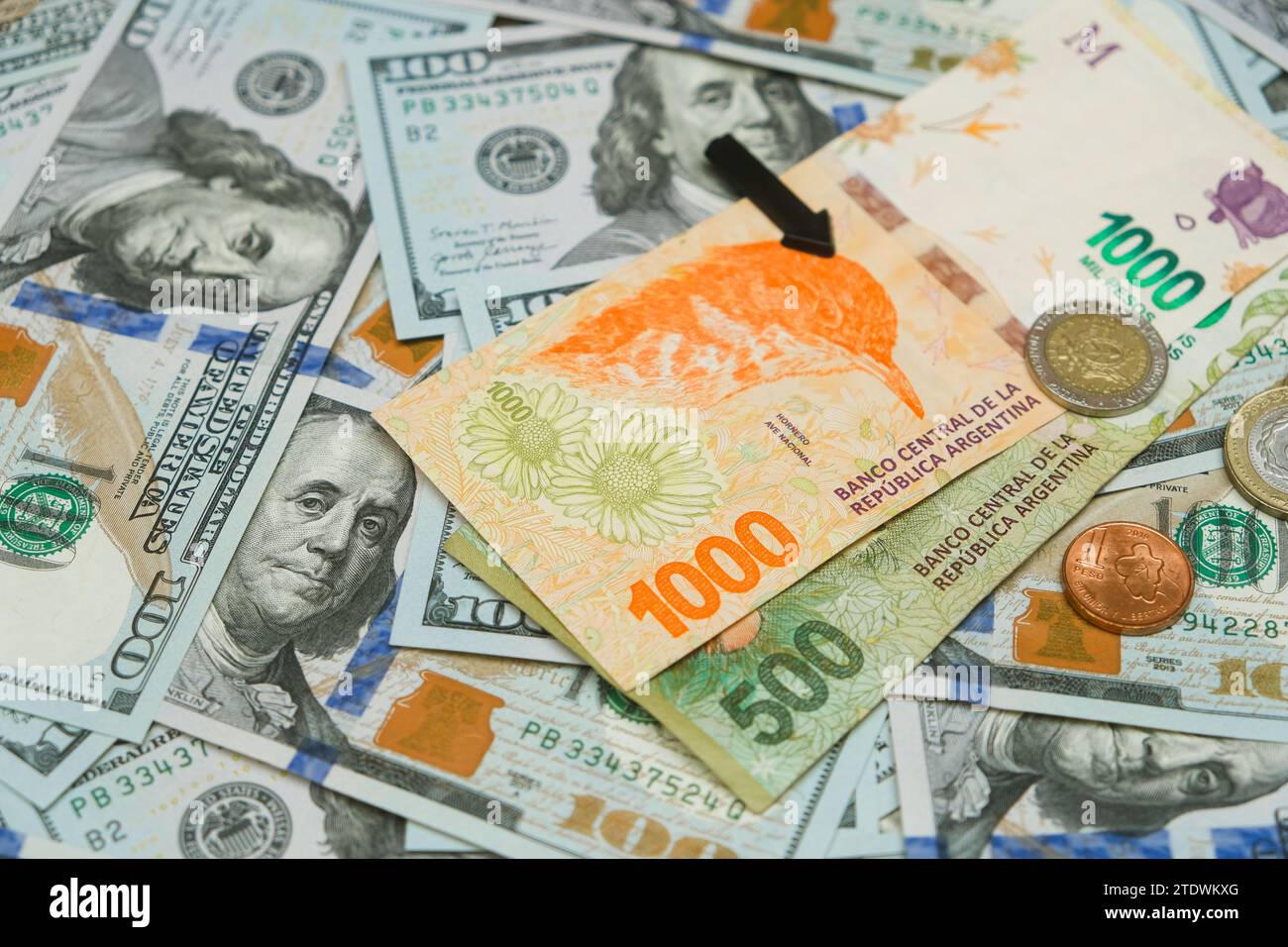 Argentine Banknotes And Coins With Black Arrow Heading Downward On US Dollars Background. Economic Situation Of Argentina. Financial Crisis Concept Stock Photo