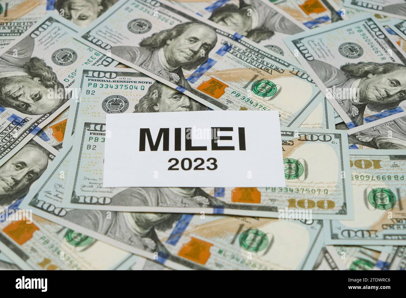 Small Paper With The Word 'Milei 2023' On A Background With Hundred Dollar Bills. Focus On The Word 'Milei' Stock Photo