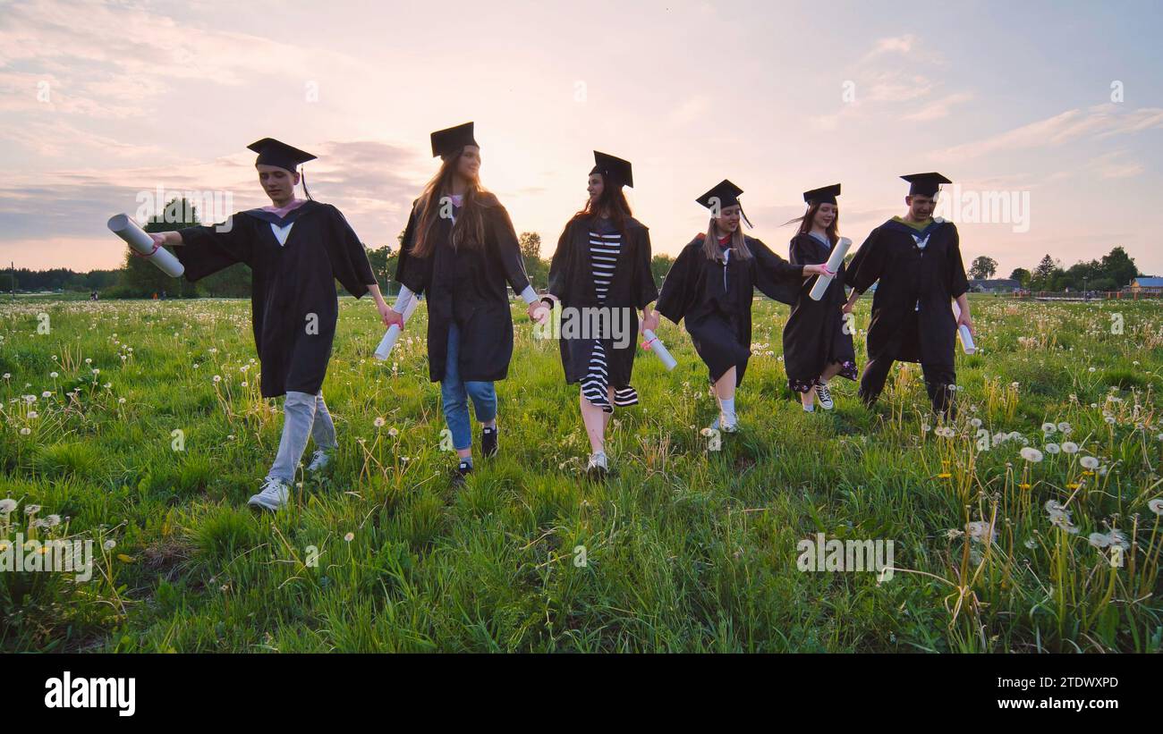 Six graduates in robes walk against the backdrop of the sunset Stock ...