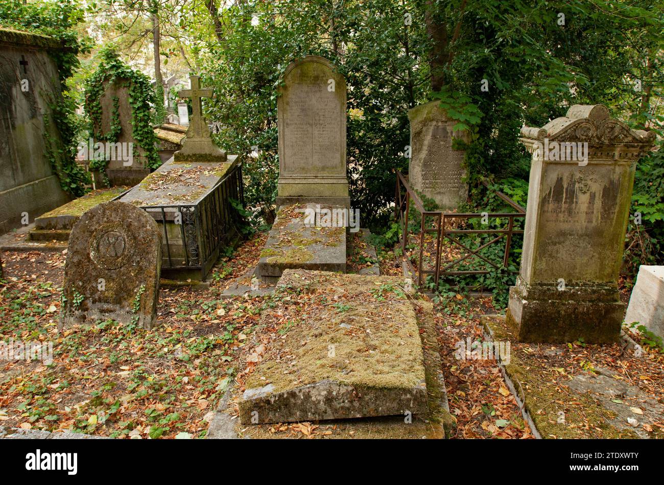 Old headstones stand covered with leaves and moss in Paris' historic Père-Lachaise Cemetery. Stock Photo