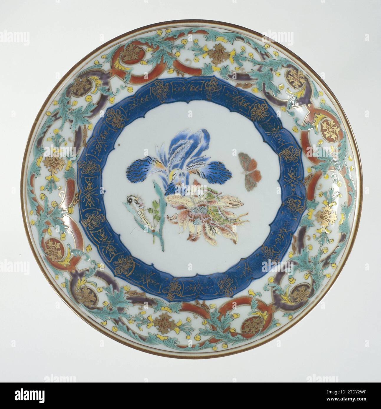 Saucer-dish with flowers, butterfly and ornamental borders, anonymous, c. 1740 - c. 1750 Scale of porcelain with round wall, painted in underly glaze blue and on the glaze in blue, red, pink, green, yellow, black and gold. On the flat two flower branches (iris, anemone) on which two caterpillars, next to it a flying butterfly; Around this a decorative tire in underly glaze blue with gold; the wall a band with a connected pattern with leaf vines; The outer edge with a tire servetwork. European performance in email colors. China porcelain. glaze. cobalt (mineral). gold (metal) painting / gilding Stock Photo