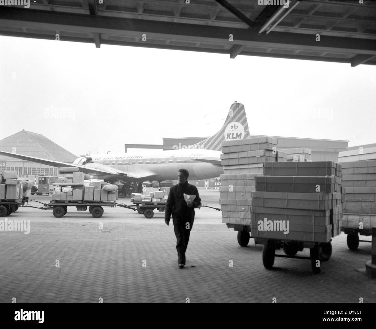 Worker in a hangar at Schiphol during the Christmas rush, KLM airplane and cargo trailer in the background ca. December 20, 1962 Stock Photo