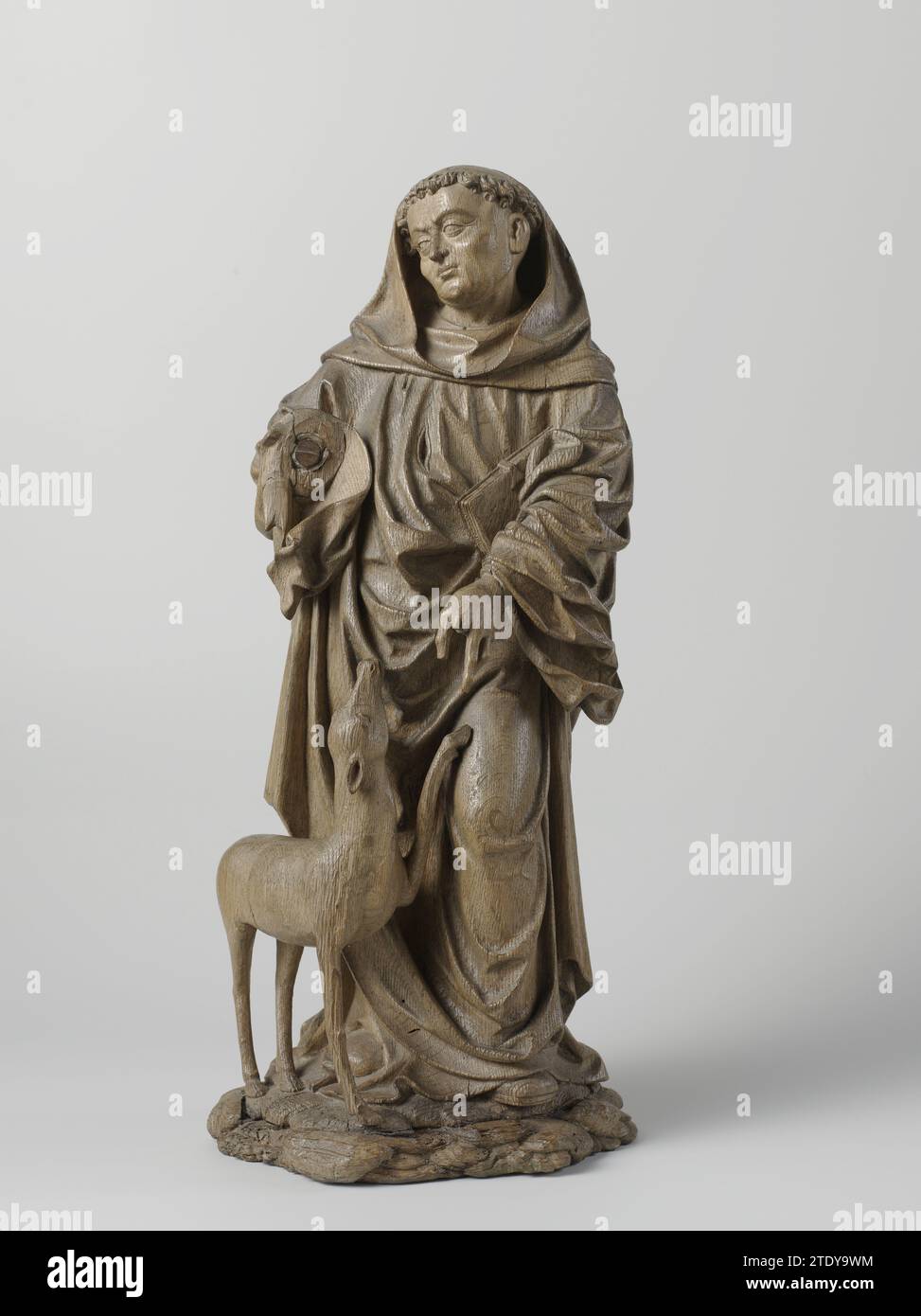 Saint Giles and the Hind, anonymous, c. 1530 - c. 1540 On a pedestal composed of pollen, he is standing forward with the bent right leg and the head diagonally to the left. He extends the left hand to the Hinde standing next to him, who looked at him and lays a front leg against Aegidius' leg. He is dressed as Benedictine, has great tonsuing, partly covered by the sagging cap of the pij, including the blunt point of the left shoe. The duck is included under the arm, including a foliant. The wound of the arrow on his chest is visible through the pip. Lower Rhine region oak (wood) On a pedestal Stock Photo