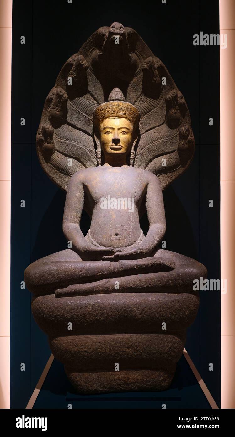 A beautiful sitting Buddah stone statue carving with a gold face and a headress of snake Nagas. Inside a gallery at the Maha Surasinghanat Building at Stock Photo