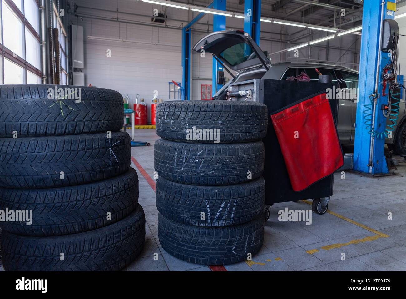 A set of tires for seasonal replacement near the lift in the tire workshop. The concept of seasonal car tire replacement. Stock Photo