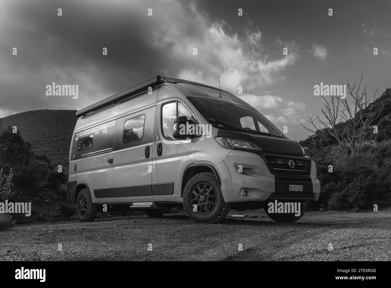 A black and white low angle view of a campervan parked on a dirt road Stock Photo