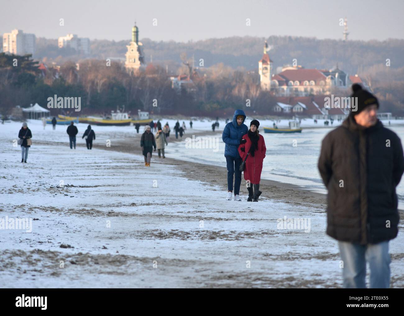 People walking along the snow covered Gdansk beach on a cold Winter day by the Baltic Sea with Sopot resort city seen in the distance, Poland, Europe, EU Stock Photo
