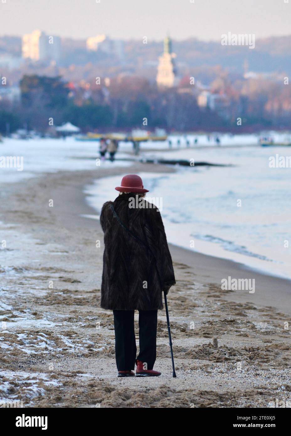 Senior woman with a cane walking towards the resort city of Sopot on the Baltic Sea coast on a snowy Winter day in Poland, Europe, EU Stock Photo