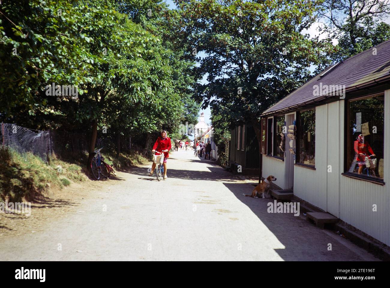 Woman cycling on main street of shops, Sark, Guernsey, Channel Islands, Great Britain, June 1974 Stock Photo