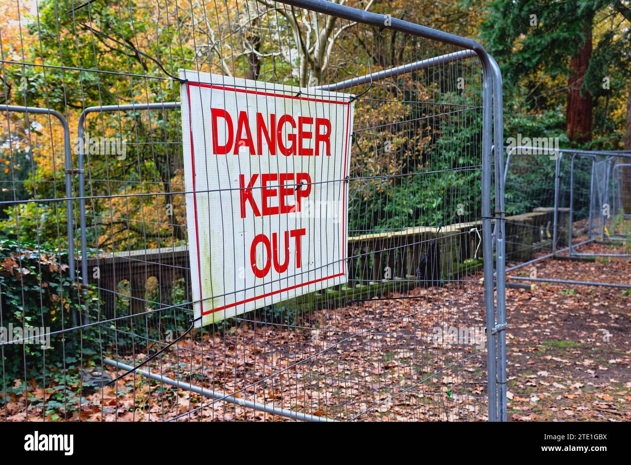A large Danger Keep Out warning sign mounted on temporary fencing in a public park with unstable parapet masonry behind Chertsey Surrey England UK Stock Photo