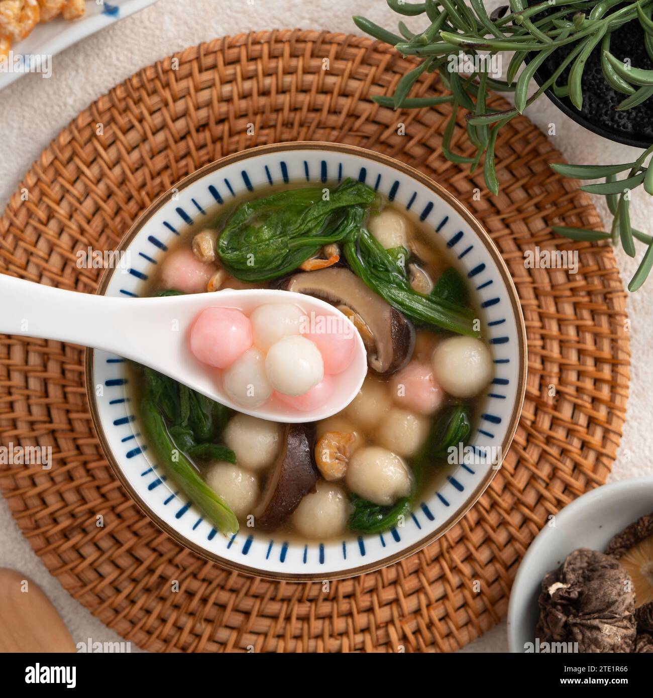 Eating homemade red and white small tangyuan, tang yuan, glutinous rice dumpling balls with savory soup in a bowl on white table background. Stock Photo
