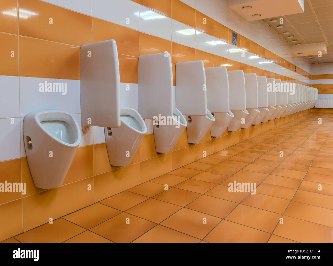 Long line of urinals in public toilet with white orange ceramic tiles ...