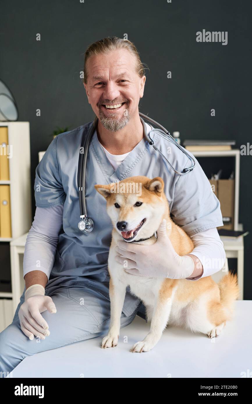 Cheerful veterinarian posing with his canine patient at vet office