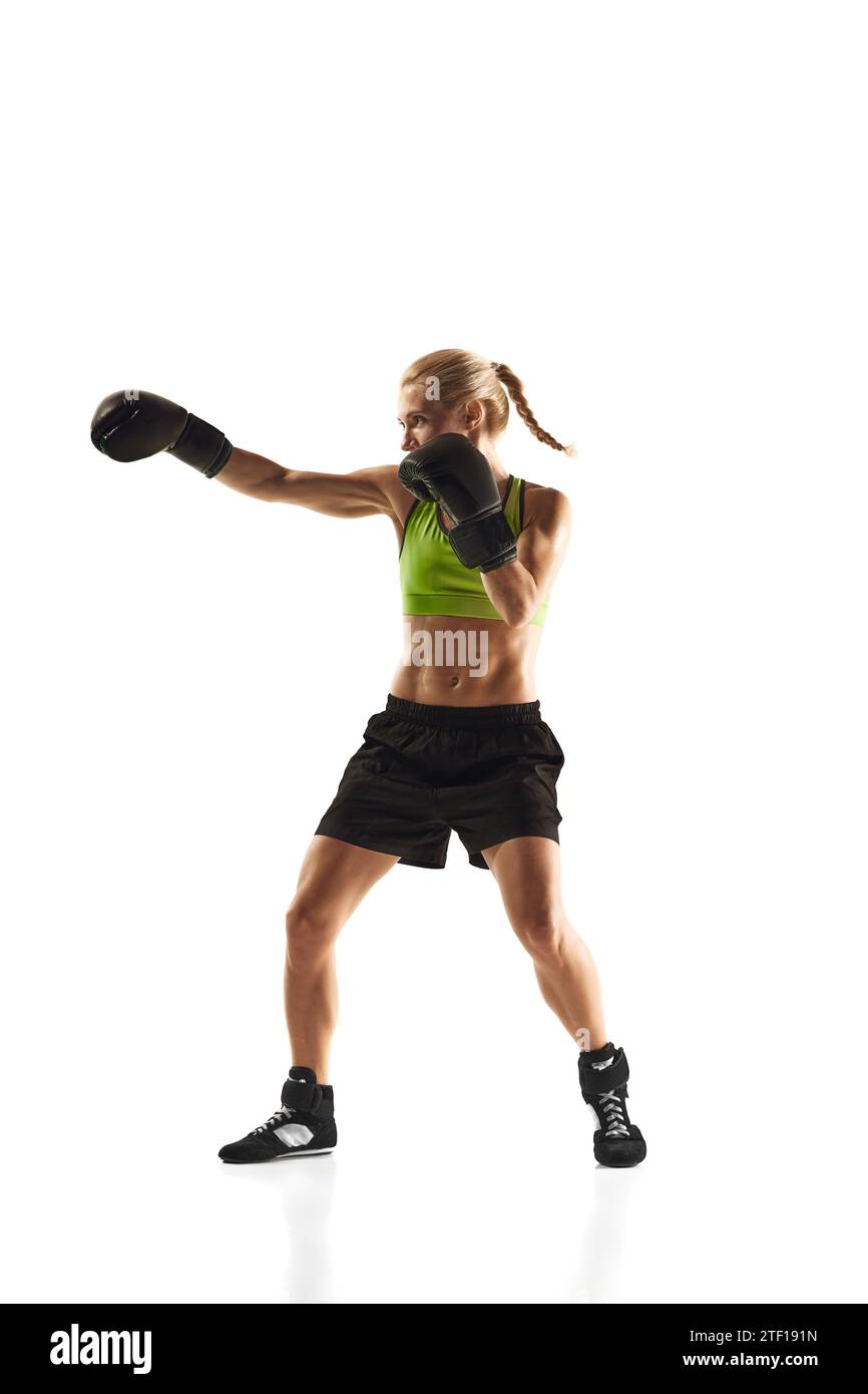 Full-length image of young woman with muscular fir body training, practicing punches isolated over white background. Sport, healthy and active Stock Photo