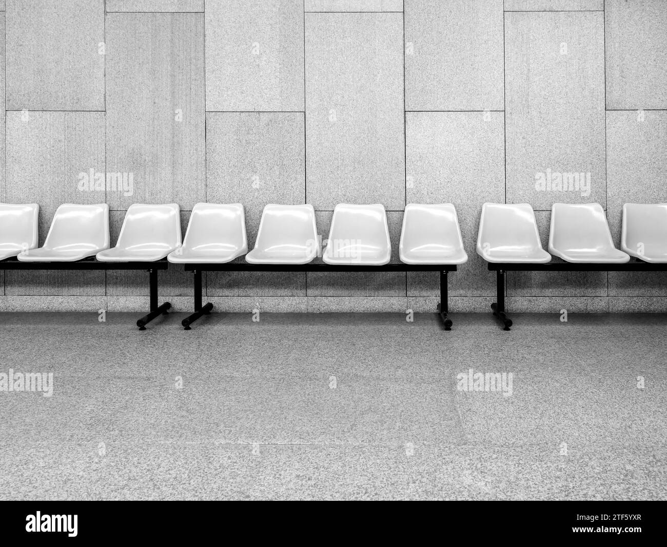 Row of empty white waiting plastic chairs seats with black iron legs seats on grey tiles and concrete wall background inside the modern building with Stock Photo