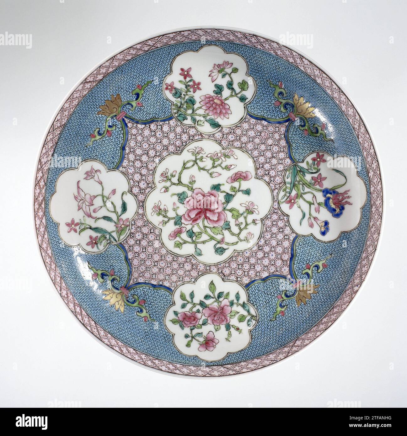 Saucer-dish with flower sprays in shaped panels on a diaper-pattern ground, anonymous, c. 1730 - c. 1745 Porcelain bowl, covered with a pink glaze and painted on the glaze in blue, red, pink, green, black and gold. On the front of the dish a lobed cartouche with a pair of pairing plant in a square scalloped cartouche with servetwork, a stylized lotus drink on the corners; On each side of the square a smaller lobed cartouche with a flowering plant (peoning, chrysanthemum, iris, balloon bell) against a ground of servetwork; On the inner edge a band with servetwork; The outside covered with a pin Stock Photo