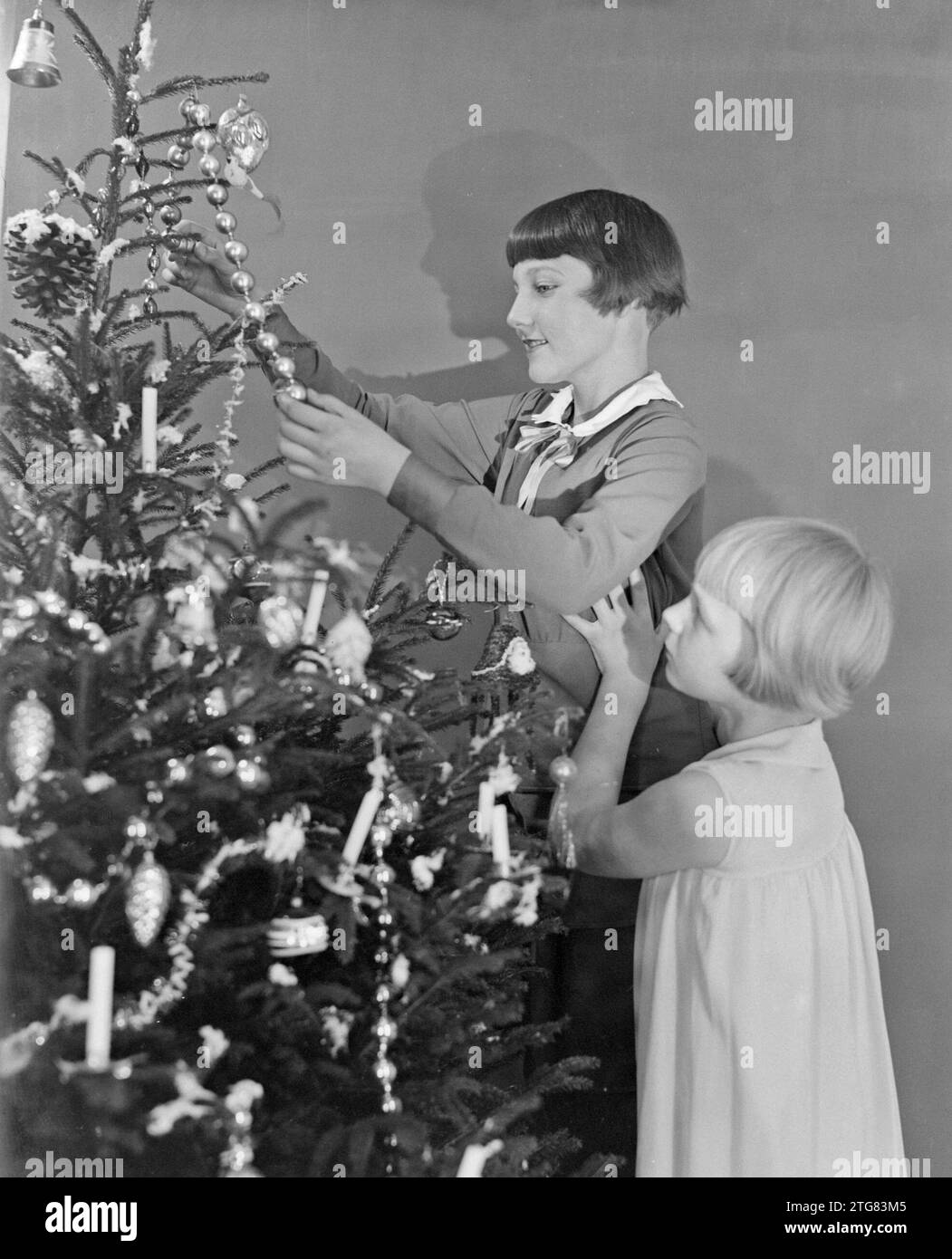Young girls look at the decorations on a Christmas tree ca. 1932 Stock