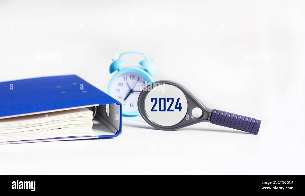 Magnifying glass with the word 2024 on a white table with a clock and a