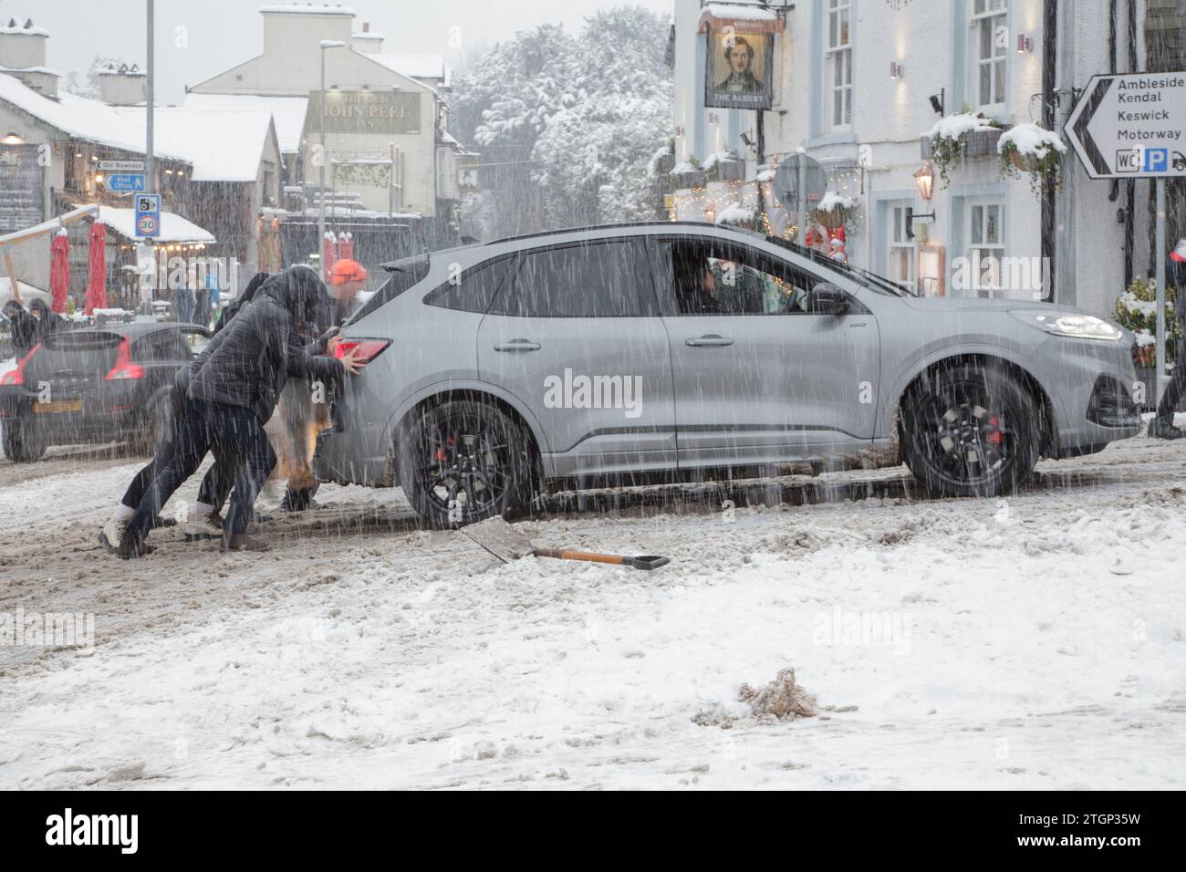Members of the public push a stranded car up an incline during a snowstorm in Windermere, Lake District Stock Photo