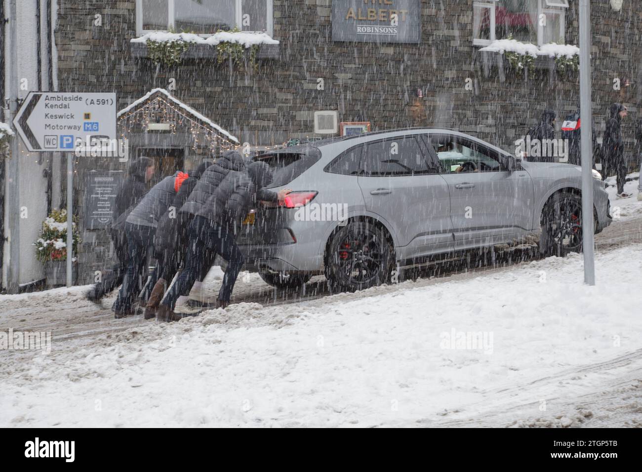 Members of the public push a stranded car up an incline during a snowstorm in Windermere, Lake District Stock Photo