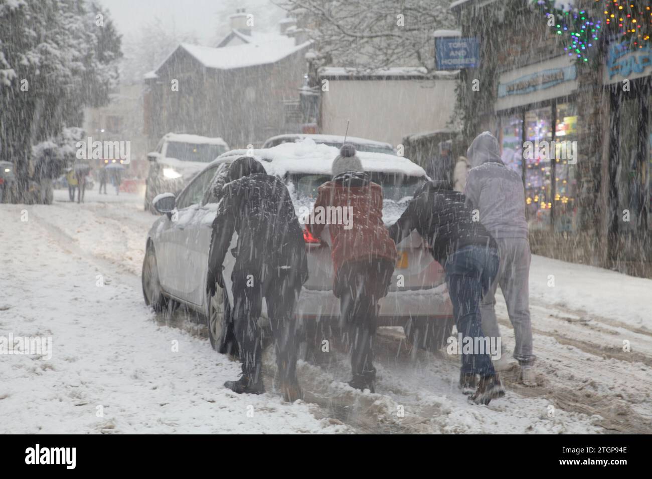 Members of the public push a stranded car up an incline during a snowstorm in Windermere, Lake District Stock Photo