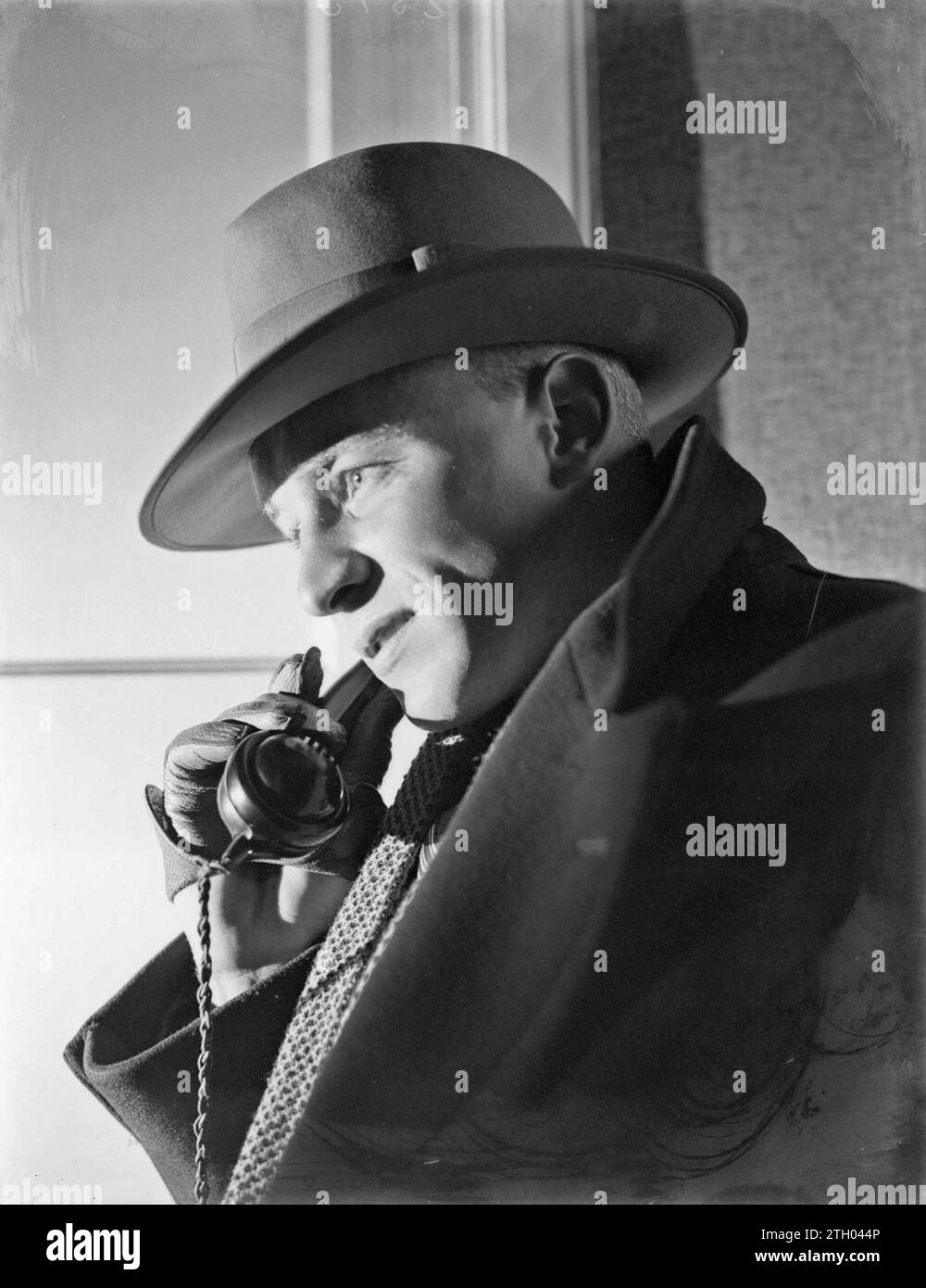 Man wearing a hat holding phone handset in gloved hand ca. 1932 Stock