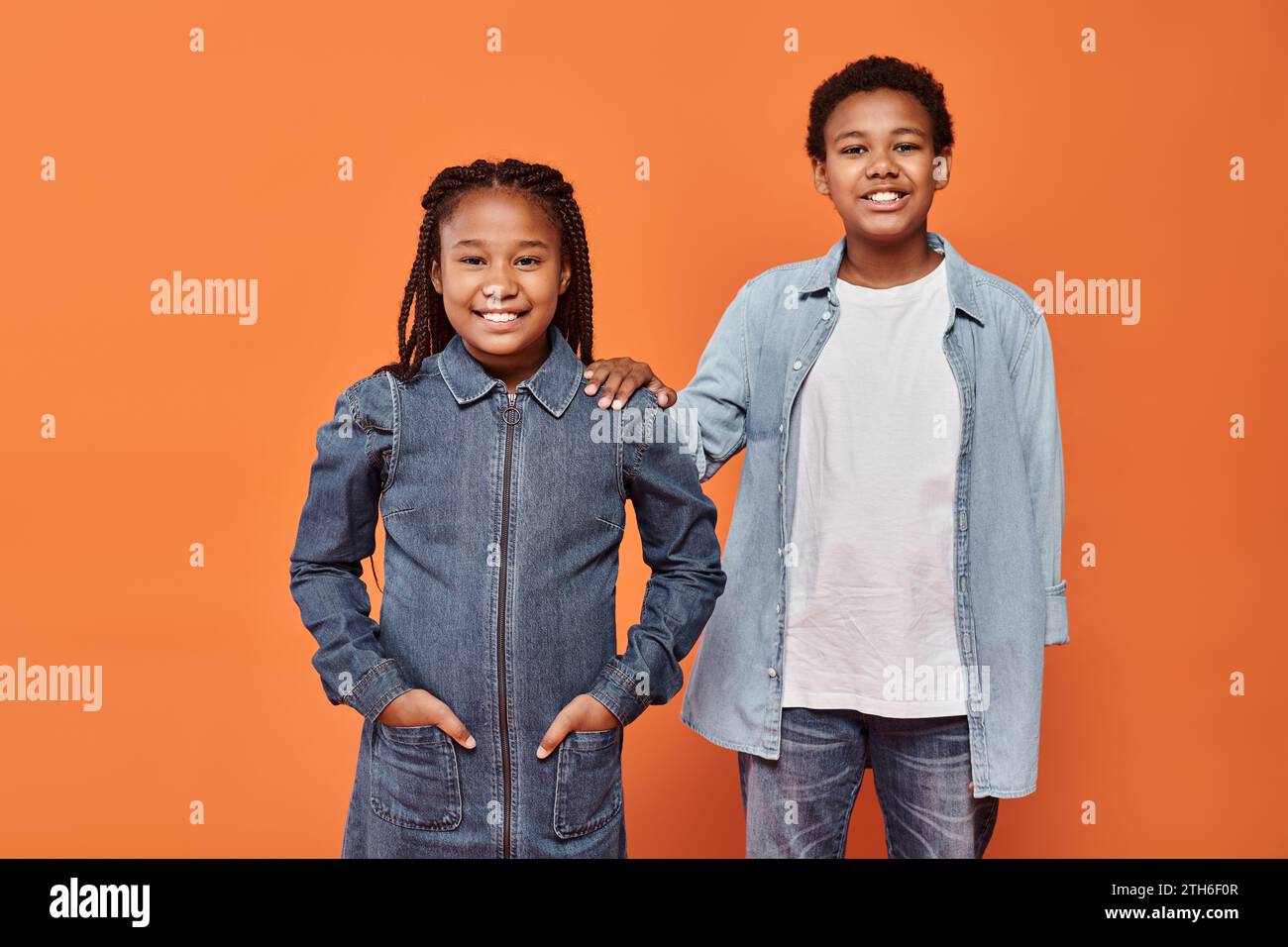 happy african american girl in casual denim attire posing together with boy on orange background Stock Photo