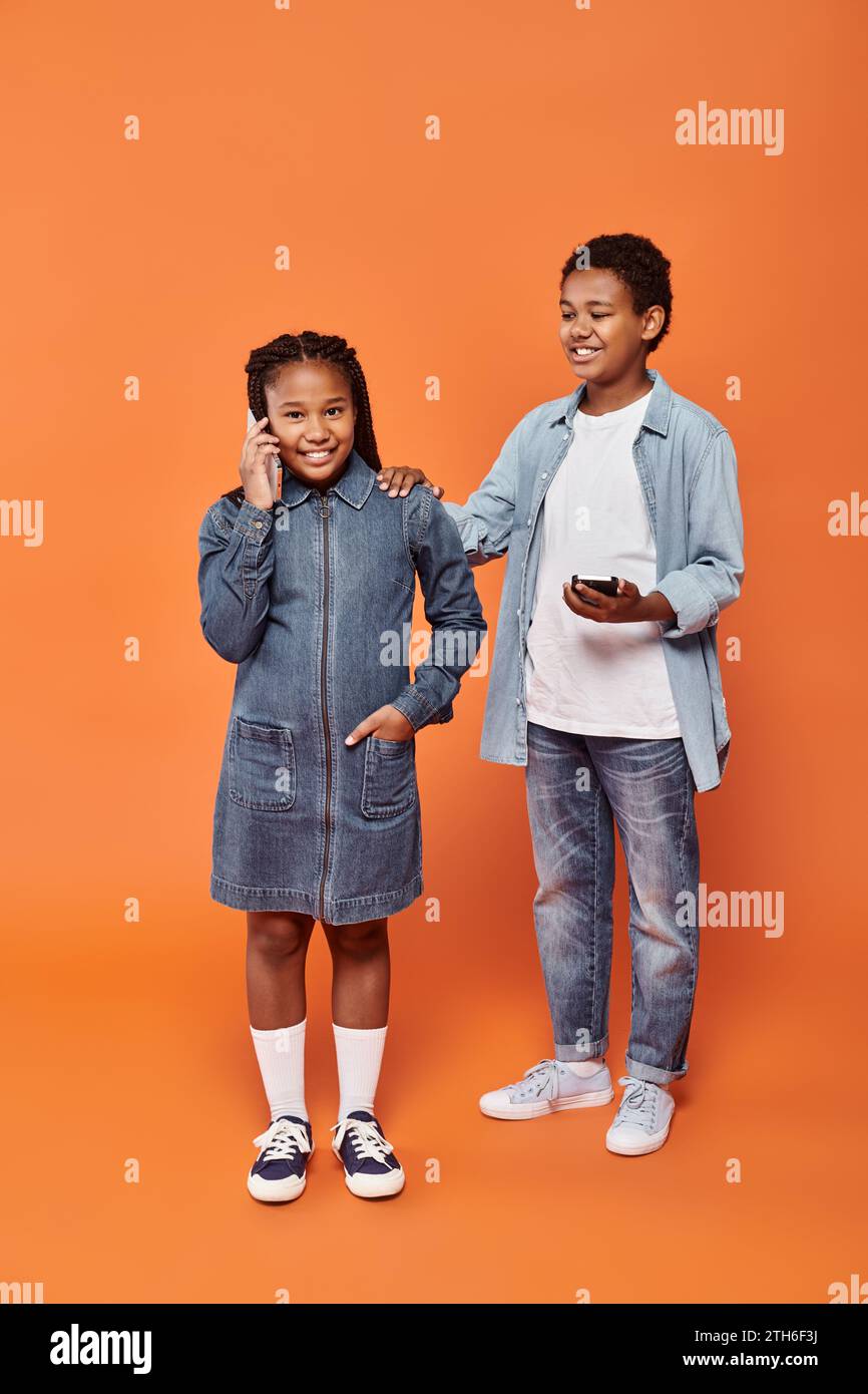 happy african american girl and boy in casual wear using smartphones on orange background Stock Photo