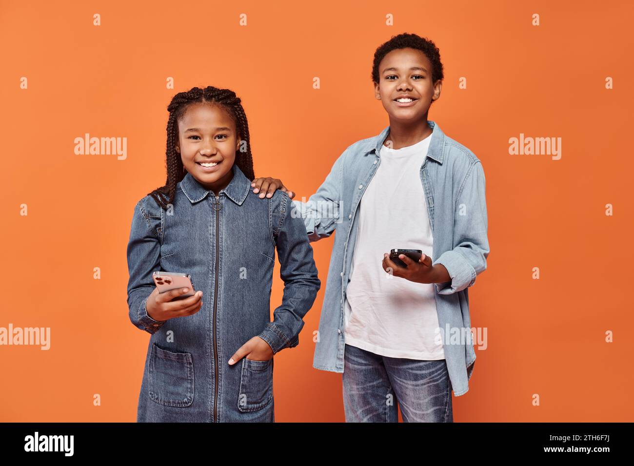 happy african american girl and boy in casual wear holding smartphones on orange background Stock Photo