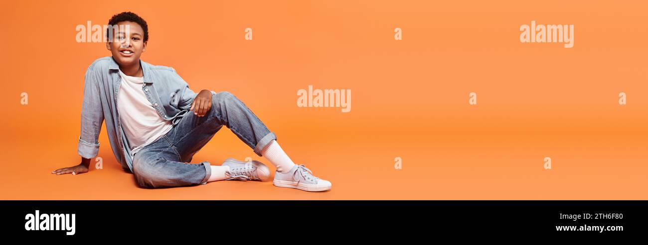 jolly preteen african american boy in casual wear posing on floor and smiling at camera, banner Stock Photo