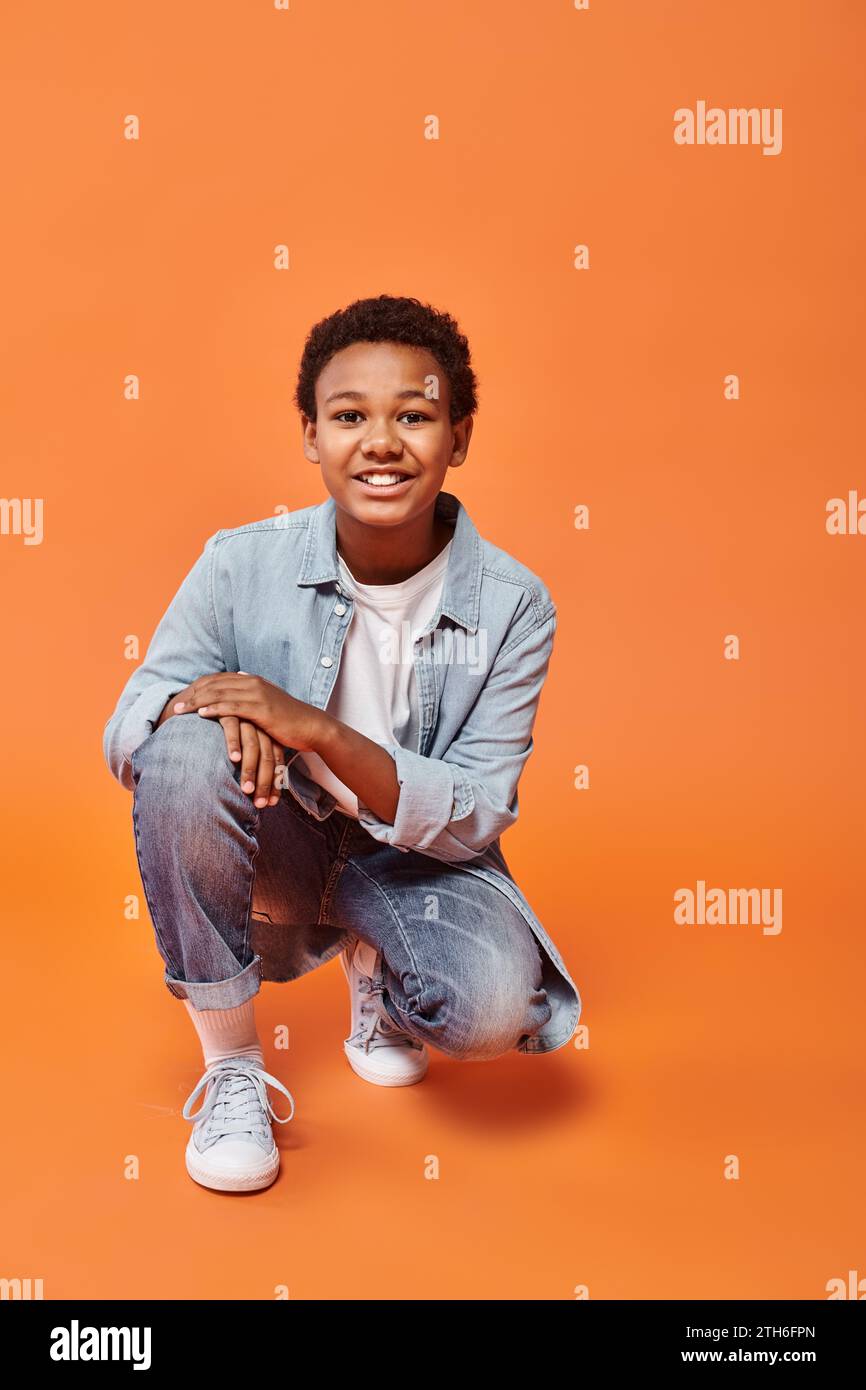 cheerful preteen african american boy in casual outfit standing on one jnee and smiling at camera Stock Photo