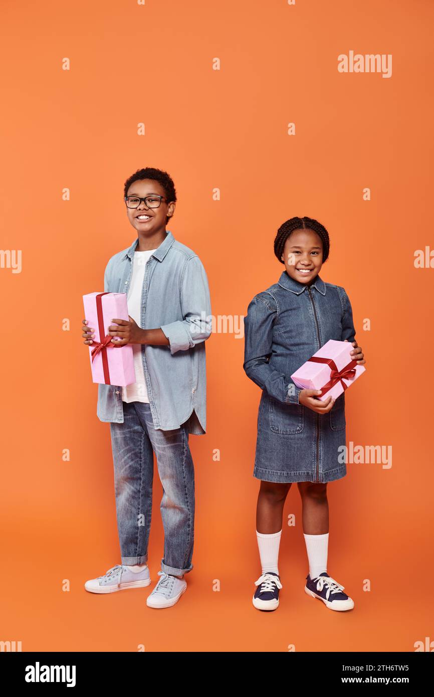 happy african american children holding wrapped presents and standing on orange background Stock Photo