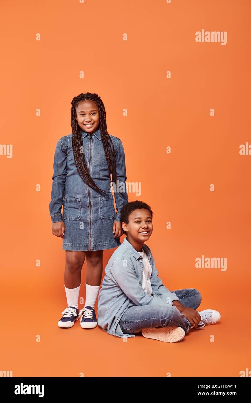 cheerful african american girl in casual denim attire standing near boy on orange background Stock Photo