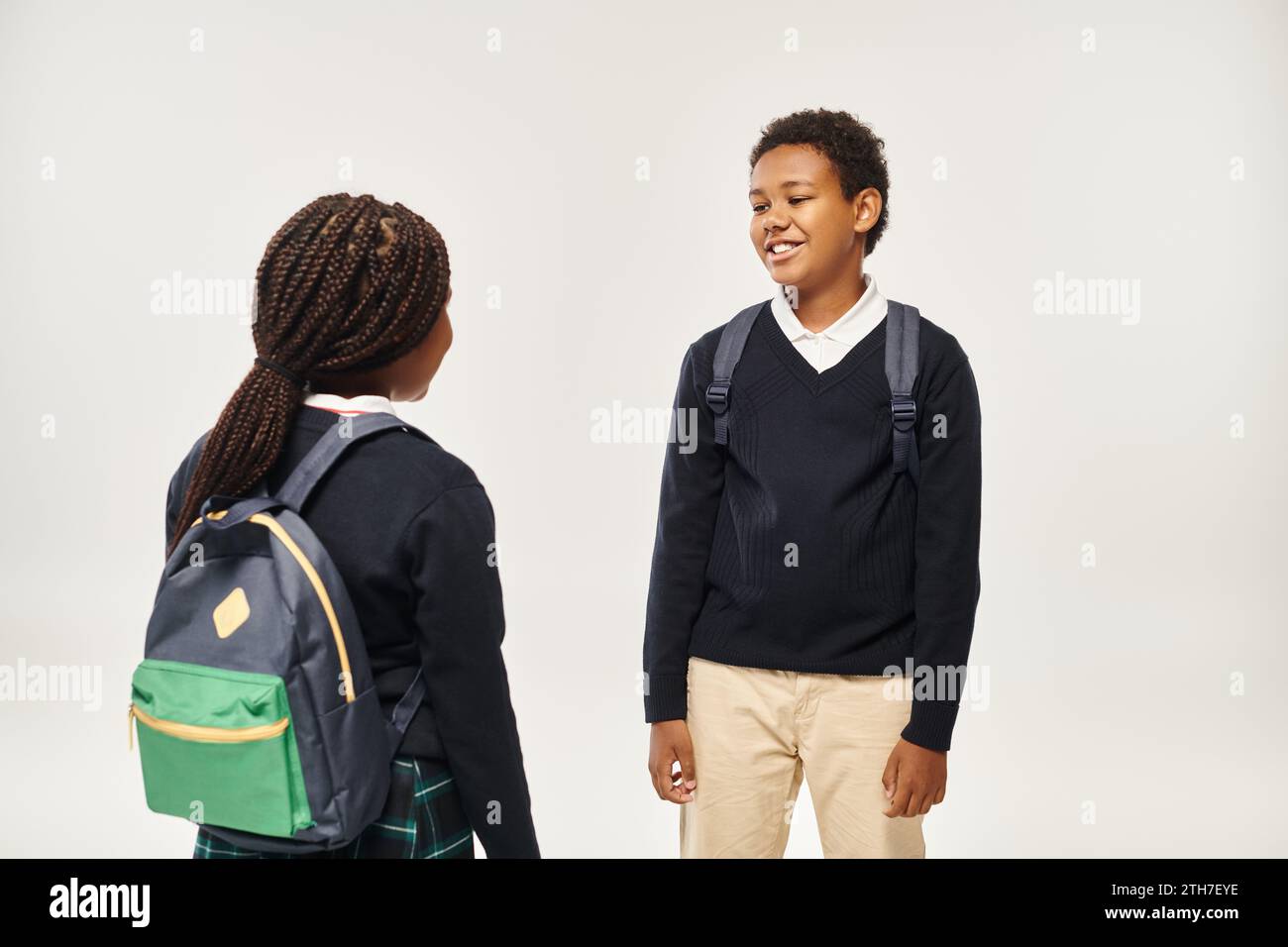 cheerful african american schoolkids with backpacks standing and chatting on grey background Stock Photo